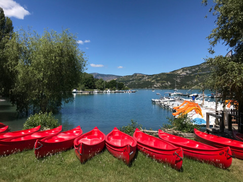 Canoas rojas alineadas en la orilla del lago de Ubaye-Serre-Ponçon, con montañas y embarcaciones al fondo.