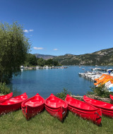 Canoas rojas alineadas en la orilla del lago de Ubaye-Serre-Ponçon, con montañas y embarcaciones al fondo.