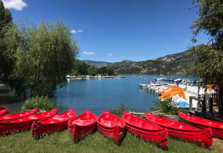 Red canoes lined up on grass by the lake in Ubaye-Serre-Ponçon, France, with boats and mountain scenery.