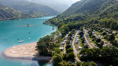 Vista aérea de un camping junto al lago en Ubaye-Serre-Ponçon, rodeado de montañas y vegetación en Francia.