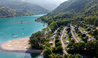 Vista aérea de un camping junto al lago en Ubaye-Serre-Ponçon, rodeado de montañas y vegetación en Francia.