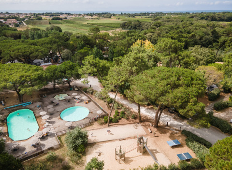 Vista aérea de piscinas, zona de juegos y vegetación en Huttopia Chardons Bleus - Ile de Ré, parque vacacional en Francia.