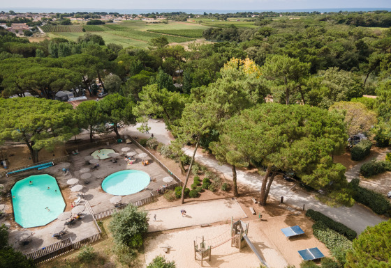 Vista aérea de piscinas, zona de juegos y vegetación en Huttopia Chardons Bleus - Ile de Ré, parque vacacional en Francia.