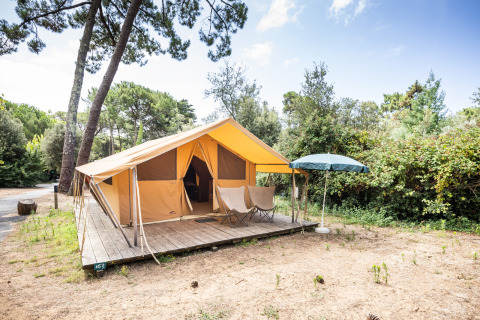 Tienda de glamping con terraza de madera y sombrilla en la naturaleza en Huttopia Chardons Bleus, Île de Ré.