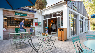 Área de cafetería al aire libre en Huttopia Chardons Bleus - Ile de Ré, con huéspedes y niños disfrutando.