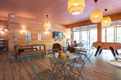Acogedor salón en Huttopia Chardons Bleus - Ile de Ré con paredes de madera, futbolín y ventanas grandes.