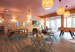 Cozy lounge at Huttopia Chardons Bleus - Ile de Ré with wood interiors, foosball table, and large windows.