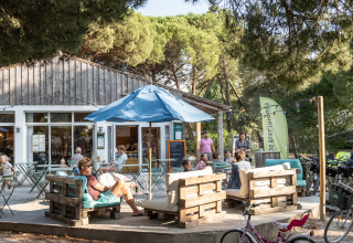Buitencafetaria met gezinnen, houten zitbanken en fietsen bij Huttopia Chardons Bleus, Ile de Ré, in het groen.