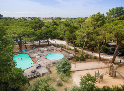 Vista aérea de piscinas y parque infantil rodeados de árboles en Huttopia Chardons Bleus, Île de Ré.