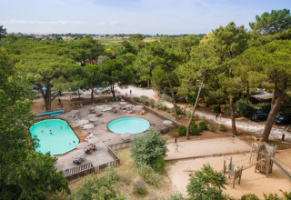 Luftfoto af poolområde og legeplads omgivet af skov i ferieparken Huttopia Chardons Bleus på Île de Ré.