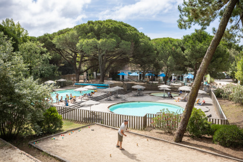 Turistas disfrutan de la piscina y juegan petanca en Huttopia Chardons Bleus - Ile de Ré en Francia.