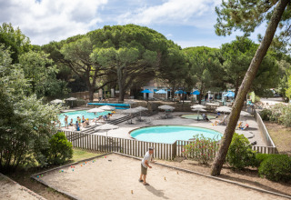 Turistas disfrutan de la piscina y juegan petanca en Huttopia Chardons Bleus - Ile de Ré en Francia.