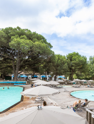 Zona de piscina con sombrillas y tumbonas rodeada de pinos en Huttopia Chardons Bleus - Ile de Ré.