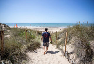 Uomo cammina a piedi nudi su un sentiero sabbioso verso la spiaggia a Huttopia Chardons Bleus - Ile de Ré, Francia.
