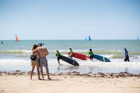 Pareja se abraza en la playa, mientras surfistas y veleros disfrutan el mar cerca de Sainte-Marie-de-Ré, Francia.