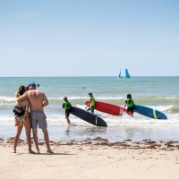 Pareja se abraza en la playa, mientras surfistas y veleros disfrutan el mar cerca de Sainte-Marie-de-Ré, Francia.