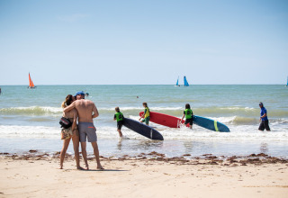 Couple embraces on the beach as surfers and sailboats enjoy the sea near Sainte-Marie-de-Ré, France.
