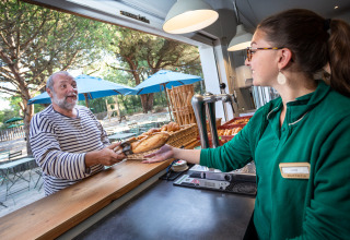 Man in gestreept shirt koopt brood aan de buitenbalie in Huttopia Chardons Bleus, Ile de Ré, Frankrijk.