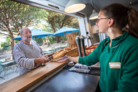 Man in gestreept shirt koopt brood aan de buitenbalie in Huttopia Chardons Bleus, Ile de Ré, Frankrijk.