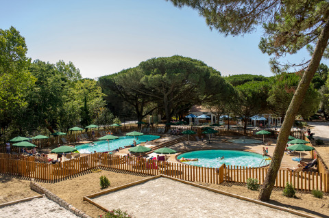 Zona de piscina al aire libre con sombrillas verdes y valla de madera en Huttopia Chardons Bleus - Ile de Ré, Francia.