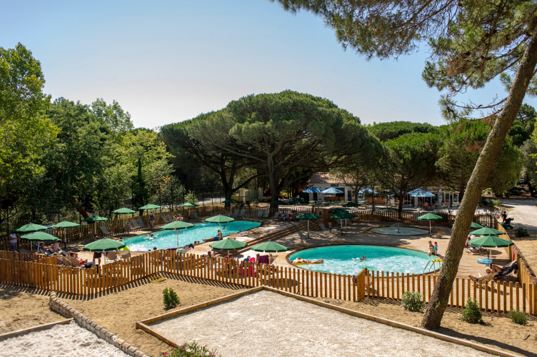 Outdoor swimming pool area with green umbrellas, wooden fencing, and guests at Huttopia Chardons Bleus - Ile de Ré.