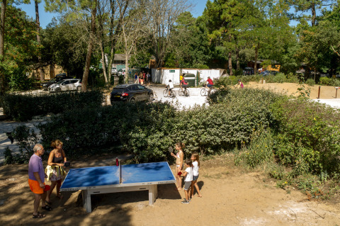 Personas juegan al tenis de mesa al aire libre en un parque vacacional rodeado de naturaleza en Huttopia Chardons Bleus, Ile de Ré.