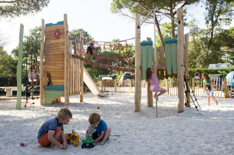 Niños juegan en un parque de arena con estructuras de madera en Huttopia Chardons Bleus – Ile de Ré en Francia.