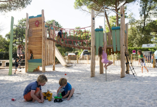 Kinderen spelen op een zandige speeltuin met houten klimrek bij Huttopia Chardons Bleus – Ile de Ré in Frankrijk.