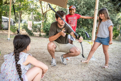 Un adulto enseña tiro con arco a niños en un campamento en Huttopia Chardons Bleus - Ile de Ré, Francia.