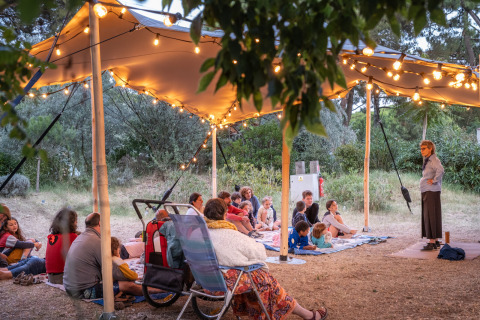 Narración al aire libre bajo una carpa iluminada en Huttopia Chardons Bleus - Île de Ré, niños y adultos atentos.