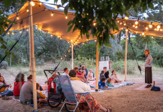 Narración al aire libre bajo una carpa iluminada en Huttopia Chardons Bleus - Île de Ré, niños y adultos atentos.