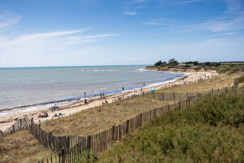Vista costera cerca de Sainte-Marie-de-Ré, Francia, con personas en la playa, dunas y mar bajo cielo azul.