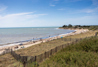 Kystudsigt nær Sainte-Marie-de-Ré, Frankrig, med folk på stranden, klitter og hav under blå himmel.