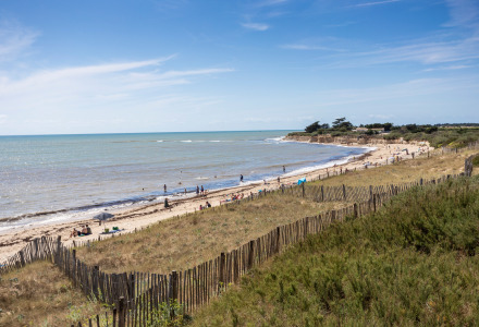 Vista costera cerca de Sainte-Marie-de-Ré, Francia, con personas en la playa, dunas y mar bajo cielo azul.