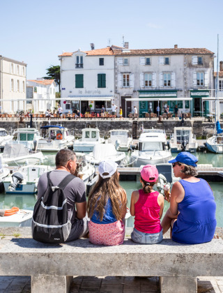 Familia sentada en un banco junto al puerto en Sainte-Marie-de-Ré, Francia, con vista a barcos y edificios.