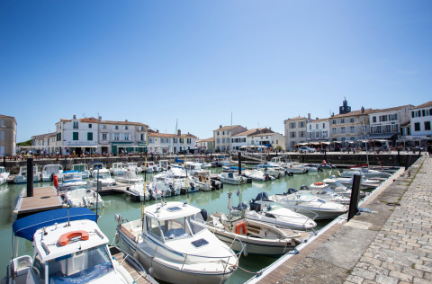 Boats docked in a scenic harbor with white houses and a holiday park offering glamping accommodations.