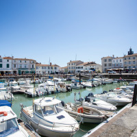 Boats docked in a scenic harbor with white houses and a holiday park offering glamping accommodations.
