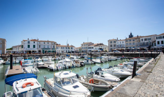 Barcos atracados en un puerto pintoresco cerca de un parque vacacional con glamping y casas blancas.