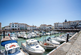 Boats docked in a scenic harbor with white houses and a holiday park offering glamping accommodations.