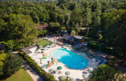 Luftfoto af en pool og legeplads omgivet af træer ved Huttopia Beaulieu sur Dordogne feriepark i Occitanie.