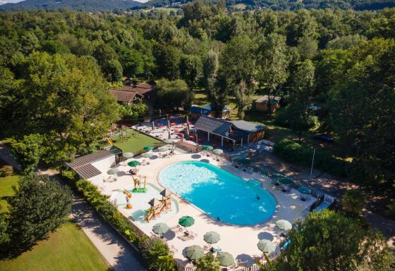 Luftfoto af en pool og legeplads omgivet af træer ved Huttopia Beaulieu sur Dordogne feriepark i Occitanie.