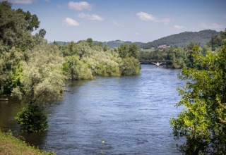 Flod omgivet af frodig grøn skov nær Beaulieu-sur-Dordogne, Occitanie, Frankrig med en bro i det fjerne.
