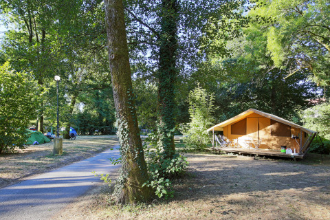 Campeggio a Huttopia Beaulieu sur Dordogne con tende, una casetta di legno e alberi verdi in Francia.