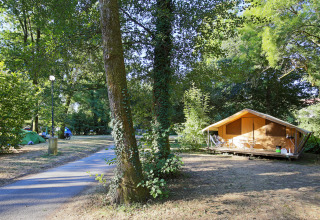 Campingplatz in Huttopia Beaulieu sur Dordogne mit Zelt, Holzlodge und vielen grünen Bäumen in Frankreich.