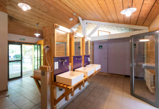 Moderne fælles badeværelsesfaciliteter med træloft på Huttopia Beaulieu sur Dordogne i Occitanie, Frankrig.