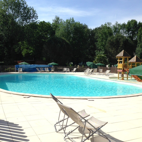 Udendørs swimmingpool med liggestole, parasoller og legeområde for børn på Huttopia Beaulieu sur Dordogne, Frankrig.