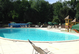 Outdoor swimming pool with deck chairs, umbrellas and children's play area at Huttopia Beaulieu sur Dordogne, France.