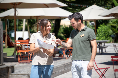 To personer diskuterer et kort i solrige udendørs omgivelser ved Huttopia Beaulieu sur Dordogne feriested.