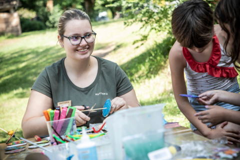Een lachende vrouw helpt kinderen met knutselen buiten op vakantiepark Huttopia Beaulieu sur Dordogne in Occitanië.