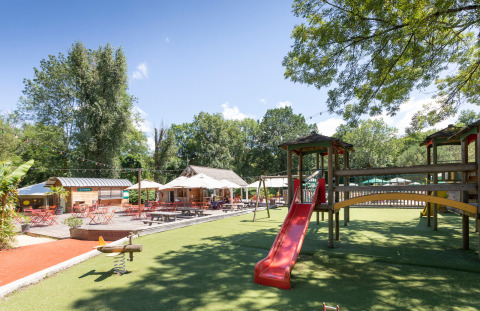 Zona de juegos y terraza al aire libre en Huttopia Beaulieu sur Dordogne, parque vacacional en Occitania, Francia.
